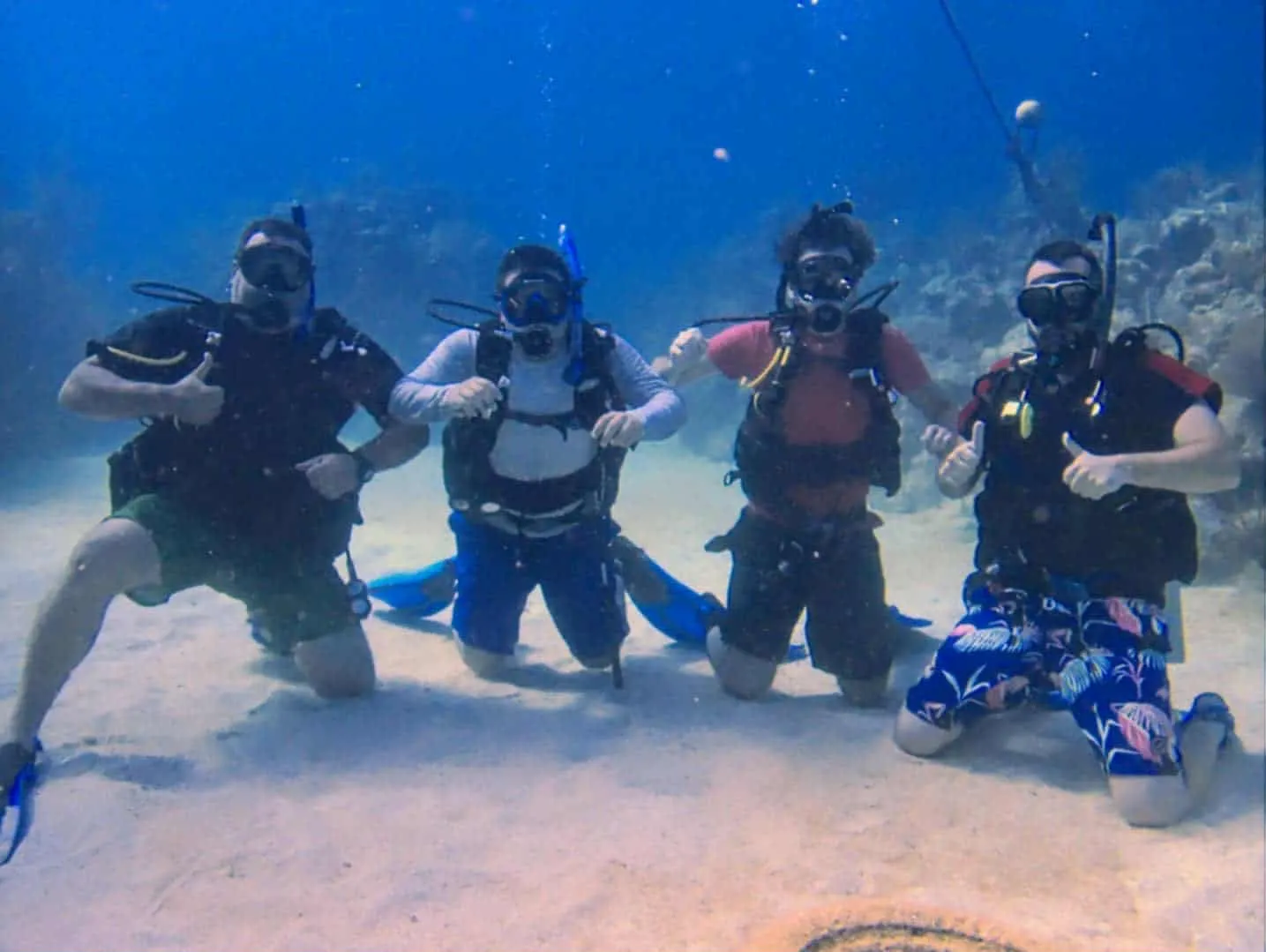 Four certified divers kneeling together on the sand underwater